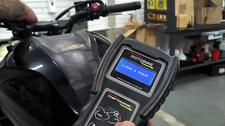 Mão de mecânico segurando um scanner para motos junto a uma moto